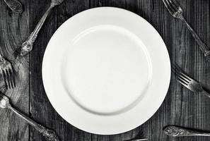 White empty plate among forks, top view photo