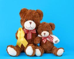 brown teddy bear sits and holds in his paw a yellow silk ribbon on a blue background photo