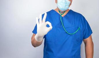 doctor in blue uniform and latex sterile gloves shows an approval symbol photo