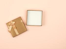 caja de regalo cuadrada dorada abierta con un lazo en un fondo beige foto