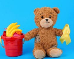 brown teddy bear sits and holds in his paw a yellow silk ribbon photo