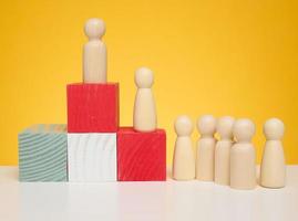 Wooden figures of men stand on a pedestal of their cubes on a yellow background. photo