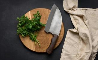 green sprigs of parsley on a wooden cutting board and a knife. Top view of black kitchen table photo