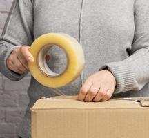 woman in a gray sweater holds a roll of duct tape and packs brown cardboard boxes photo