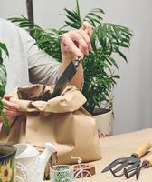 A woman in gray clothes holds a bag of soil for planting seeds in paper cups. Hobby and leisure photo