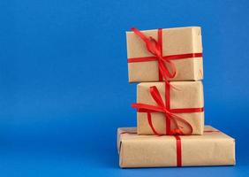 stack of boxes wrapped in brown paper and tied with a red bow, gifts on a blue background photo