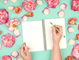 female hand holds a white pen over empty white sheet of paper photo