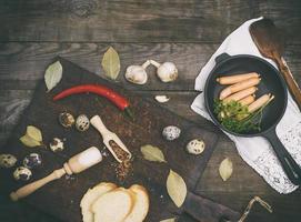 sausages in a black round cast-iron frying pan and raw quail eggs photo