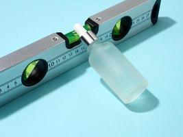 white glass bottle with a pipette lies on a building level on a blue background photo