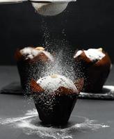 baked chocolate muffin on a black table sprinkled with powdered sugar photo