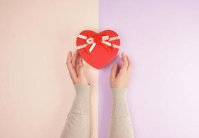 two hands hold a paper closed red box in the shape of a heart photo