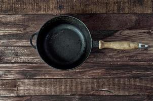 Black cast-iron frying pan on a brown wooden surface photo