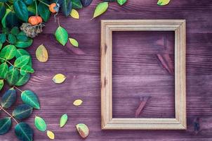 Empty wooden frame on brown wood surface among green and yellow leaves photo