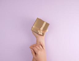 women's hands hold a closed box with a bow on a purple background photo