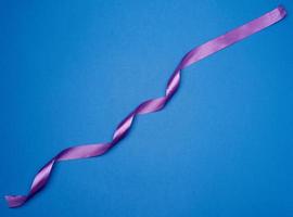 purple silk thin ribbon twisted on a blue background photo