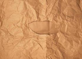 crumpled brown sheet of paper with a hole, in the middle of a brown background photo