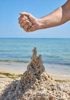 la mano construye un castillo de la arena mojada del mar foto