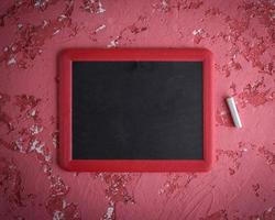 an empty black chalk board in a red frame and a piece of chalk photo