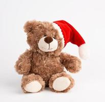 cute brown teddy bear in a red christmas hat sits photo