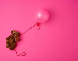 pequeño oso de peluche marrón sosteniendo un globo inflado rosa en una cuerda foto