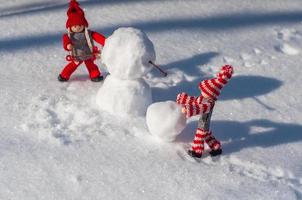 dos pequeños hombres de madera en la escena de construir un muñeco de nieve entre la nieve blanca pura foto