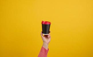 hand holds paper cardboard brown cup for coffee, yellow background. Eco-friendly tableware, copy space photo