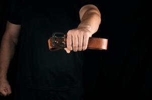 man in black clothes is holding a brown leather belt with a buckle photo