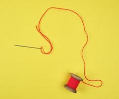 wooden reel with red wool thread and a large needle photo