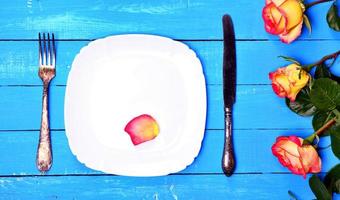 White plate with knife and fork on a blue wooden background photo