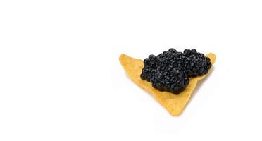Triangular nachos with black paddlefish caviar isolated on white background. Snack photo