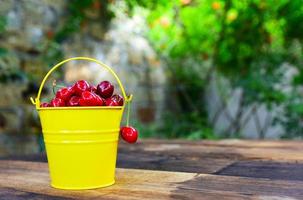 Red cherry in a yellow bucket on a brown wooden table photo