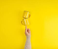 two yellow ceramic cups are supported by a female hand on a yellow background photo