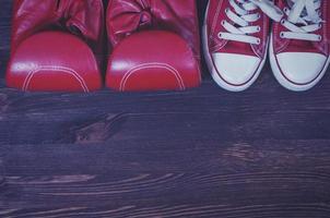 Red boxing gloves and a pair of red sneakers on a brown wooden surface photo