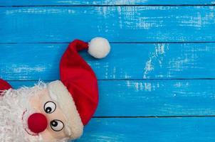 Smiling Christmas Santa Claus in a red cap on blue wooden surface, empty space on the right photo