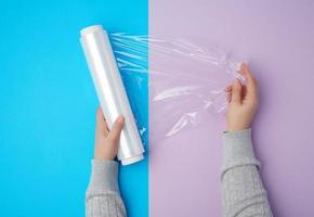 two hands hold a large roll of wound white transparent film for wrapping food photo
