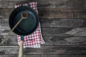 Black frying pan with a wooden spoon on a brown wooden surface photo