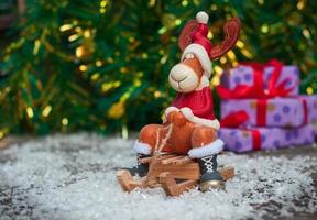 ciervos de juguete de navidad en ropa de vacaciones en trineo de madera entre la nieve foto