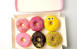 six round different donuts with sprinkles in a paper white box photo