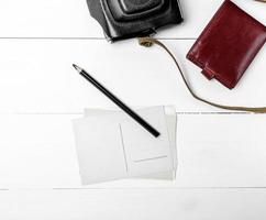 empty paper postcards and a black wooden pencil on a white wooden background, beside a brown leather purse photo