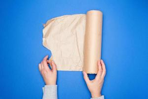 two hands holding a roll of brown parchment paper on a blue background, photo