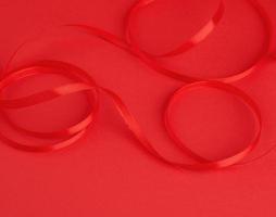 twisted red silk shiny ribbon on a red background photo