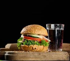 cheeseburger with grilled beef patty, cheddar cheese, tomato and lettuce on a wooden board, black background photo