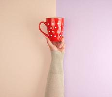 female hand holding a red ceramic mug with white polka dots photo