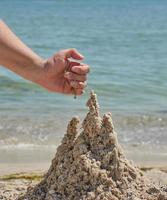 mano construye un castillo de la arena mojada del mar en la playa foto