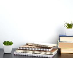 stack of spiral notebooks with white pages and ceramic pots with plants on a black table photo