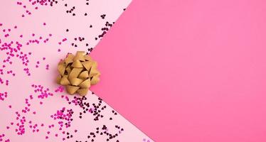 golden bow and shiny multi-colored round confetti scattered on a pink background photo