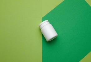 white plastic jar for pills, cream and medicines on a green background. Container for substances, top view photo