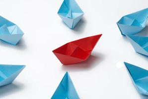 blue paper boats around the red one in the center. The concept of uniting around a strong leader. Bullying and conflict in the team photo