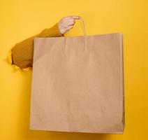 Woman holding in hand brown blank craft paper bag for takeaway on yellow background. Packaging template photo