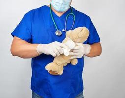 doctor in blue uniform bandages white medical bandage paw brown teddy bear photo
